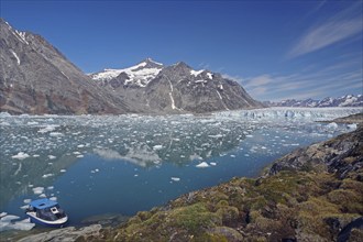 A small boat moored on a clear fjord in front of an impressive mountain and glacier landscape, Knud