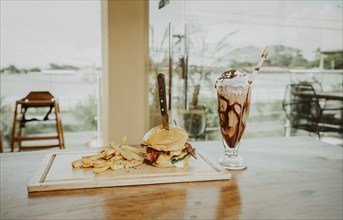 Delicious big burger with french fries and milkshake on restaurant table. Close up of burger with