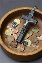 Crucifix with coins and buttons in a wooden bowl, church and money