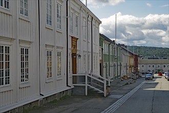 A quiet city street with light-coloured wooden buildings and a cloudy sky in the background, Unesco