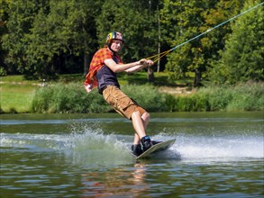 Young casual man with flapping shirt on wakeboard in lake, water ski and wakepark, Stráž pod