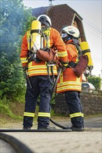 Two firefighters in orange uniform and breathing apparatus standing together, fire brigade,