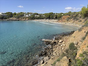 View of a beach with clear water, surrounded by trees and rocks in sunny weather, Cala Llenya,