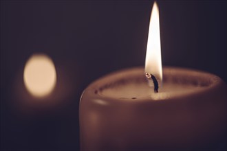 A burning candle in a dark environment radiates a warm and cosy atmosphere