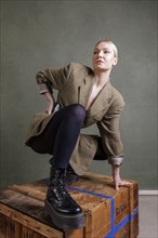 Woman in fashionable clothes posing on a wooden box in front of a green background, photo shoot