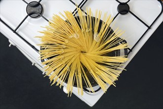 Top view of a pot with boiling water on the stove, with uncooked spaghetti noodles placed upright.