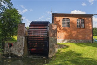 A large waterwheel next to a brick building in a green setting, engine house with waterwheel to