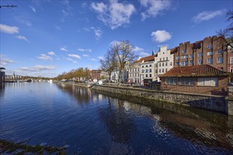 River Trave, historic houses, blue sky with fair weather clouds, quay wall, street An der