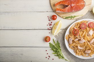 Semolina pasta with salmon and salmon steak on a white wooden background and linen textile. Top