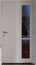 A burglar stands in front of an entrance door in the dark with a gun and looks through the glass