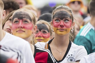 Women wearing make-up in the German national colours watch the football match in the fan zone at