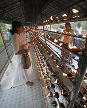 Sri Lankan pilgrims pour oil into candle holders at the Buddhist Temple of the Tooth or Sri Dalada