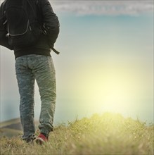 Low angle of backpacker man walking in the countryside. Rear view of backpacker man walking in the