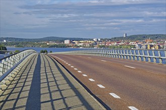 Bridge leading to a city over water with blue sky and clouds, buildings in the background,