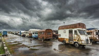 An abandoned row of old, rusty mobile homes under a threatening, cloudy sky after the rain,