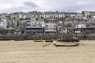 A wide beach with boats on the sand at low tide and a bustling town in the background under a