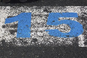 High angle view and close-up of big blue painted number 15 on white painted rectangular background