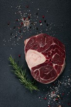 A shank on the bone, raw meat for ossobuco, on the table, with a branch of rosemary, top view, no