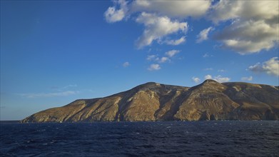 Rocky coast of an island under blue sky and light clouds, Kassos Island, neighbouring island