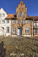 Historic brick building, façade with gable, windows, door and wall anchor, cobblestones, street An