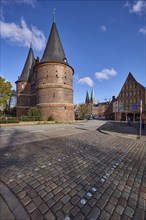 Lübeck Holstentor, side view, pedestrian crossing, cobblestone pavement, blue sky with fair weather