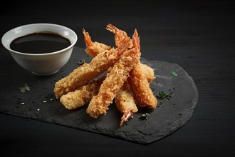 Shrimp in tempura, deep-fried, on black slate, with soy sauce, horizontal, no people