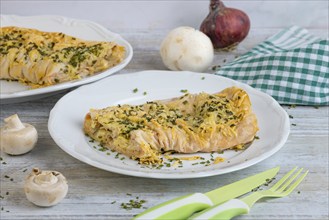 Ready-made savoury strudel with cheese and ham served on a plate, decorated with herbs