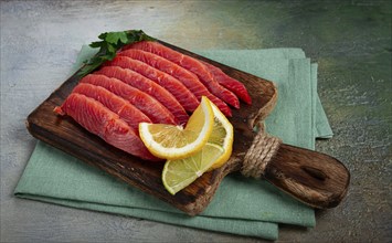 Chum salmon, cold smoked, sliced, on a cutting board, with lemon and parsley, top view, close-up,