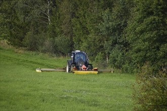 Farmer with a Valtra tractor mowing at the edge of a forest with 3 mowers at the same time,