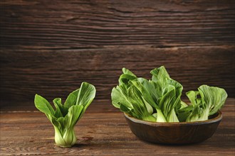 A collection of vibrant bok choy in a rustic wooden bowl on a wooden kitchen table, with one