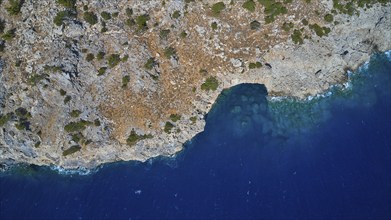 Drone shot, aerial view of a coast with rocks and a small sea cave at the blue water, drone shot,