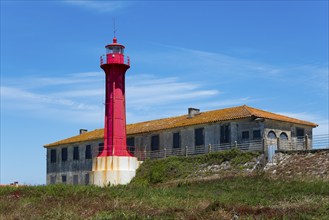 Red lighthouse next to a building in a coastal landscape with blue sky, Farol de Esposende in front