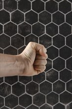 A strong fist is positioned in front of a textured hexagonal pattern, showcasing tension and