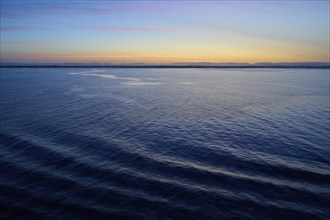 Calm sea under orange blue sky at sunrise with gentle waves, Sunrise, Bergen, Vestland, Norway,