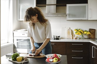 Young housewife peeling fresh organic beet while making meal in the kitchen