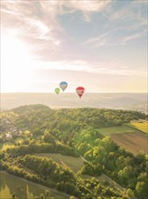 Hot air balloons hovering over farmland and forest in a hilly landscape at sunset, Calw, Black