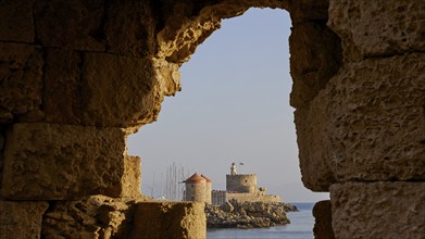 View through a stone opening to a lighthouse by the sea in the morning light, windmills, Fort of