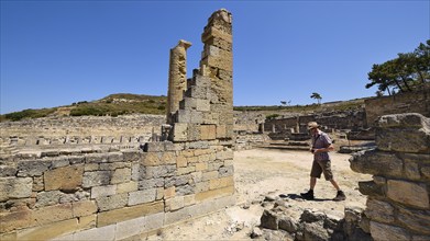 Man walking through a site with ancient stone ruins under a clear sky, Kamiros, Archaeological