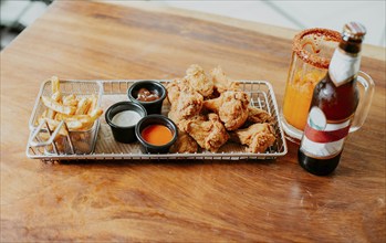 Top view of spicy wings with fries and michelada accompanied with beer served on wooden table