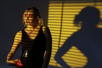 Woman standing in shadow in front of yellow light, modern and mysterious flair, photo shoot