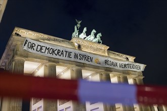 A banner For Democracy in Syria / Defend Rojava hangs behind a police barrier at the Brandenburg