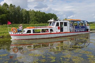 A white and red passenger boat sails along a quiet canal, surrounded by green nature, Zefir ship,