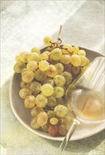 A branch of white grapes, on a gray plate, with a glass of white wine, top view, natural light,