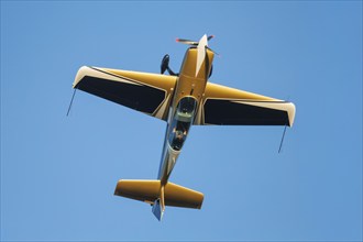 Golden stunt aerobatic plane performing stunts in blue sky. Concept of speed, difficulty,