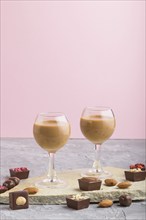 Sweet chocolate liqueur in glass with chocolate candies on a gray and pink background and stone