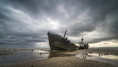 An abandoned shipwreck lies on the beach under a threatening, stormy sky, symbol photo, AI