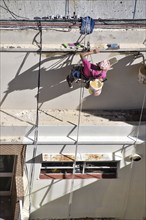 Painter hanging from a rope while working on a façade, symbolic image for safety in construction,