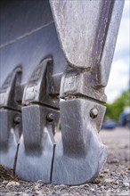 Close-up of the serrated metal teeth of an excavator with clear signs of wear, demolition site,