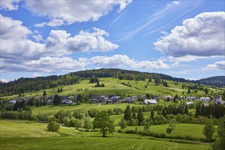 Landscape with hills, forest and meadows under a blue sky with cumulus clouds as seen from the