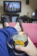 Couch potato, lazy man in comfy chair with pint of beer wearing worn slippers with big toes